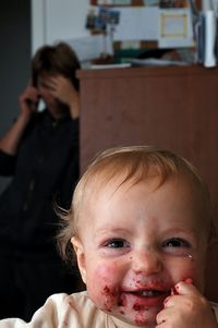 Close-up portrait of toddler with messy face sitting against mother talking on phone