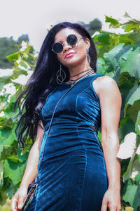 Beautiful young woman wearing sunglasses standing against plants