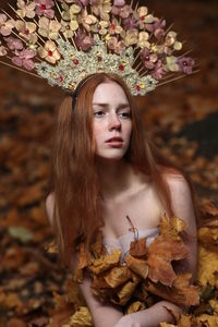 Thoughtful young woman wearing flowers on hair sitting at forest during autumn