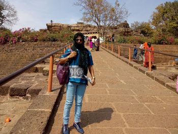 An indian lady, standing behind the sky, wearing blue top and jeans, with a stole, 