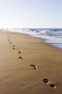 Footprints on sand at beach against clear sky