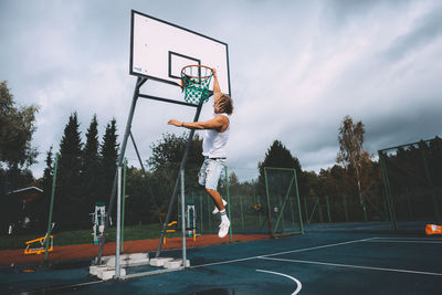 Man playing with basketball hoop against sky