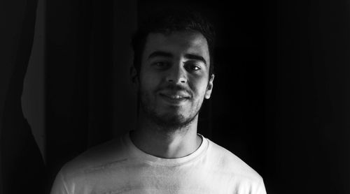 Portrait of young man standing against black background