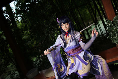 Side view of young woman standing against trees