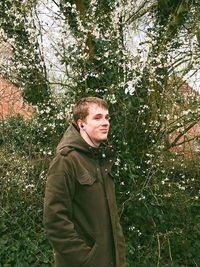 Young man standing by tree in forest