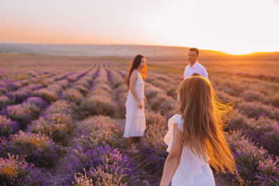 Rear view of woman walking on field against sky during sunset