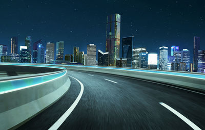 Illuminated road by buildings against sky in city at night