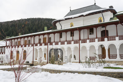 Snow covered house by building against sky