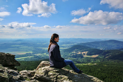 Side view of woman sitting on cliff against landscape