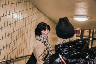 Smiling young woman wearing warm clothing while looking at friend in subway