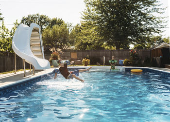 Boy looking at brother jumping in swimming pool on sunny day