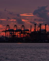 Silhouette cranes at commercial dock against sky during sunset