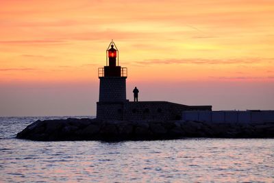 Lighthouse by sea against sky during sunset