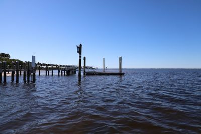 Wooden posts in sea against clear sky