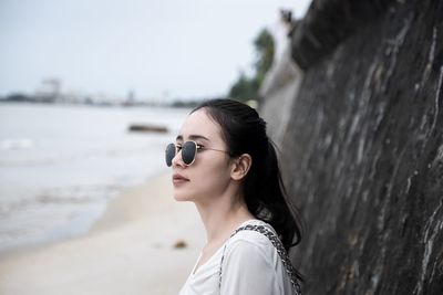 Young woman wearing sunglasses while standing by stone wall at beach