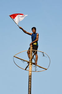 Low angle view of person holding flag while standing on pole against clear blue sky
