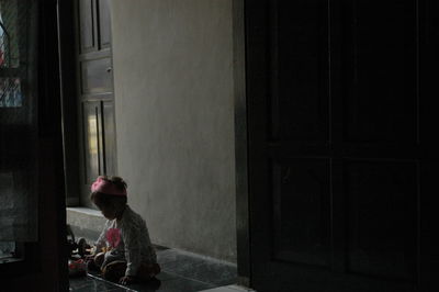 Rear view of little girl sitting on window at home