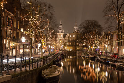 Boats moored on canal by illuminated houses at night