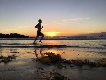 Silhouette man on beach against sky during sunset