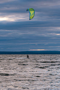 Person paragliding in sea against sky