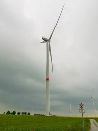 Low angle view of wind turbines on field against sky