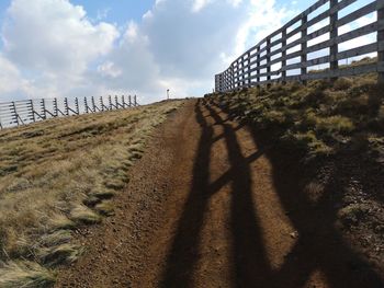 Shadow of fence on field against sky