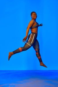 Low section of woman with arms raised against blue background