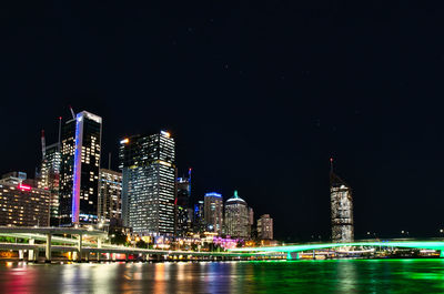 Illuminated buildings by river against sky at night