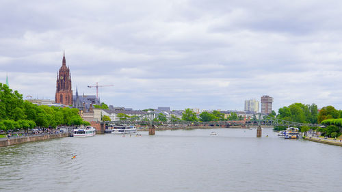 Buildings by river against cloudy sky