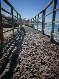 Shadow of railing on beach against sky