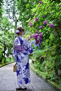 Rear view of woman standing on footpath by flowering plants