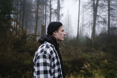 Side view of man looking way while standing in forest