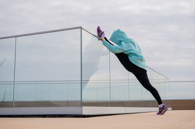 Caucasian woman in a sweatshirt stretches on the twine outdoors. 