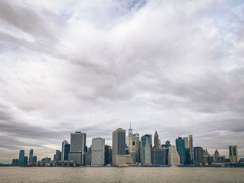 View of new york city skyline from brooklyn pier park buildings in city against cloudy sky