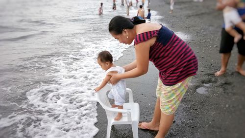 Side view of mother holding daughter standing on chair at beach