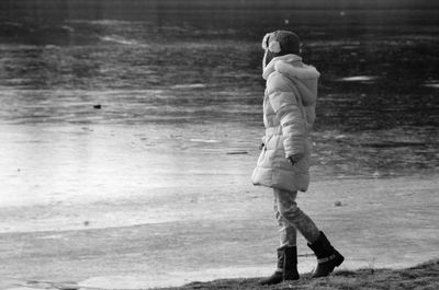 Side view of woman wearing warm clothing while walking at lakeshore