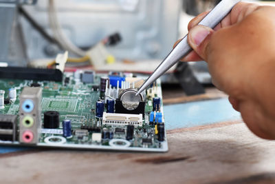 Cropped hand of technician repairing mother board at work shop