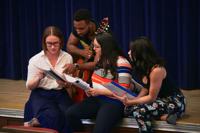 Multi-ethnic students reading music sheets on stage in auditorium