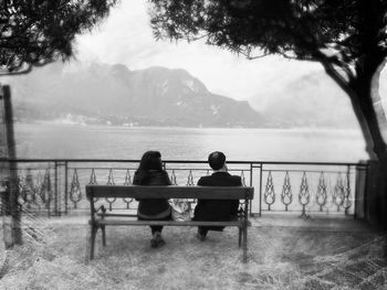 Rear view of man sitting on bench by lake