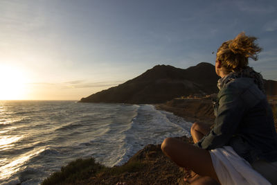 Woman looking at sea against sky during sunset