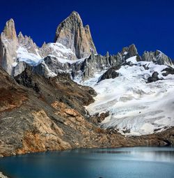 Scenic view of lake and snow covered mountains against clear blue sky