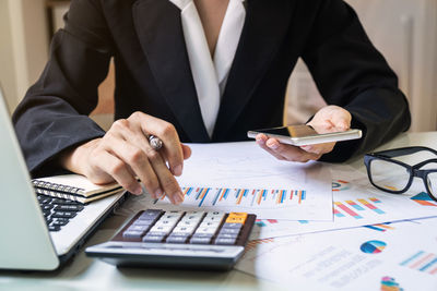 Midsection of businesswoman using smart phone while calculating on desk