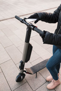 Low section of teenage girl unlocking e-scooter while scanning mobile phone on street