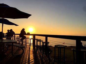 Silhouette people by railing against sea during sunset