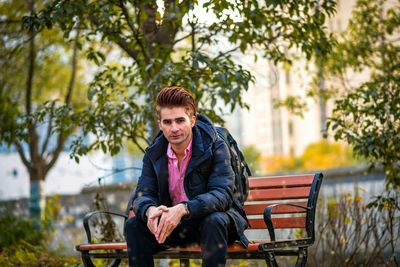 Side view of young man sitting on bench in park