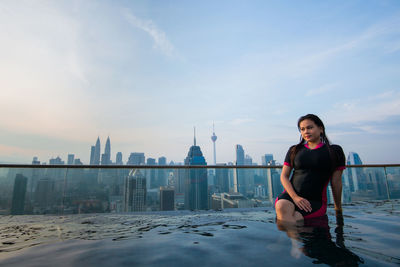 Thoughtful woman sitting in infinity pool against city