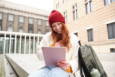 Portrait of young woman using laptop while sitting in city