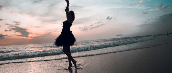 Woman standing on beach against sky during sunset