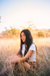 Young woman sitting on field against sky during sunset