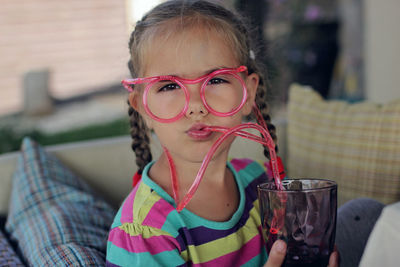 Cute girl in funny red eyeglasses used like straw drinking water from a glass on the open terrace